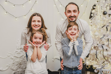 Funny photo of funky positive mom, dad and siblings posing, making grimaces over glittering new year background.