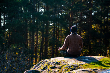 Man in a sweater meditates on a rock against the forest.