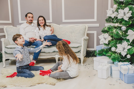 Little boy and girl conjuring snowflakes with their hands, while parents looking at them, sitting on the sofa.