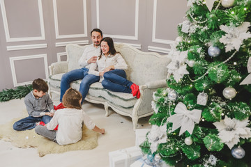 Picture of dad, mom and daughter at home near the Christmas tree, all are smiling. Children are playing on the forefront.