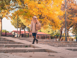 Fototapeta premium view from behind of a young traveling girl with hat, boots and backpack, taking a walk on an autumn afternoon