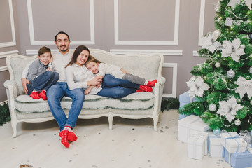 Loving parents and little children want to have photo near Christmas tree, they are posing and giving thumbs up.