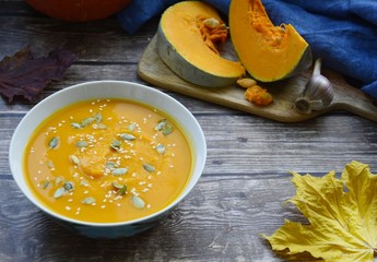 pumpkin soup in a deep plate, slices of pumpkin on a cutting board and yellow maple leaf on a gray wooden background with space for text.  f