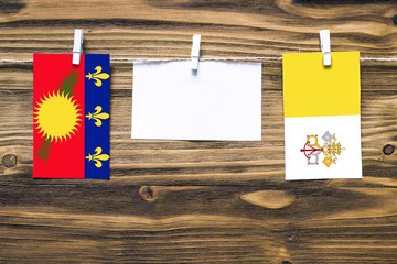 Hanging flags of Guadeloupe and Vatican City attached to rope with clothes pins with copy space on...