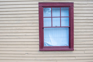 Lone red window on a yellow building with wood siding.