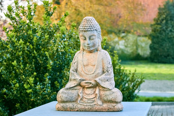 Buddha statue with closed eyes in the lotus position against the background of bushes. Old clay buddha statue