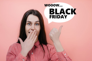 Portrait of stupefiied young woman stares at camera, covering opened mouth with palm, points with index finger at upper right corner. Concept black friday, cyber monday, purchases, sales, finance.