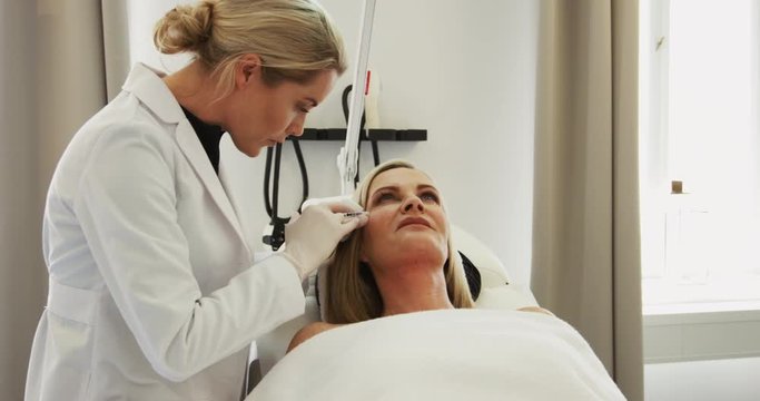 Doctor injecting botox into a mature woman's forehead 