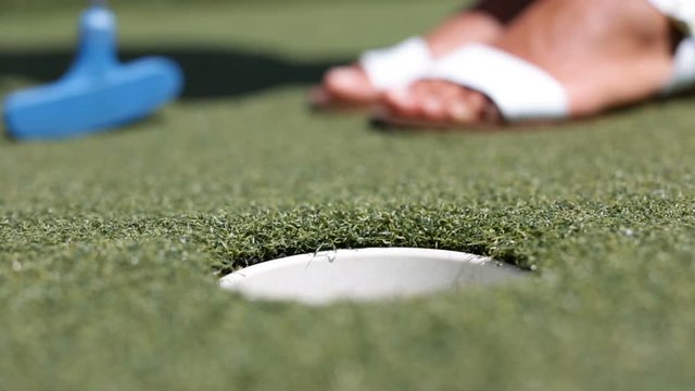 Mini golf or Miniature golf, also known as minigolf, mini-putt, crazy golf, or putt-putt. - woman putting with golf club ball in hole.