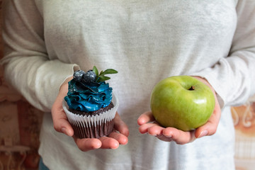 green apple and sugar cupcake in the hands, the dilemma of what to choose, the concept of healthy eating and lifestyle, the problem of diet weight loss and overweight
