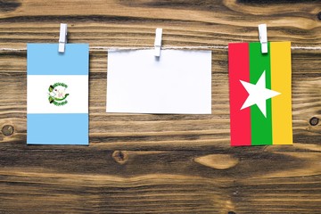 Hanging flags of Guatemala and Myanmar attached to rope with clothes pins with copy space on white note paper on wooden background.Diplomatic relations between countries.