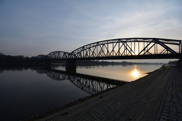 Fototapeta na wymiar Truss bridge against sunset reflecting on the river below