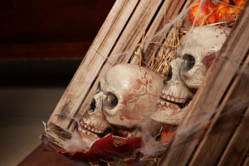 Imitation of two human skulls in a box with a straw and pumpkins. Symbol of death and evil. Halloween interior decoration. Copy space.