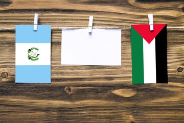 Hanging flags of Guatemala and Palestine attached to rope with clothes pins with copy space on white note paper on wooden background.Diplomatic relations between countries.