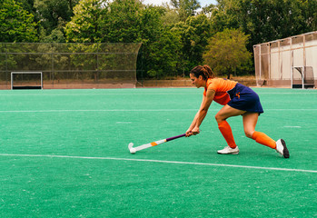 Female hockey player attacking and hitting on a grass field.