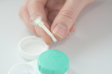 the girl is holding a container for soft contact lenses and a lens on her finger