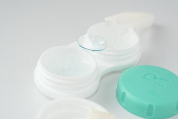 container for soft contact lenses and lens on light background