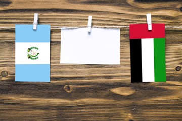 Hanging flags of Guatemala and United Arab Emirates attached to rope with clothes pins with copy space on white note paper on wooden background.Diplomatic relations between countries.