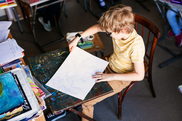 Blonde boy with glasses drawing. Group of elementary school pupils in classroom on art class. Paper with white free space for text. Russia, Krasnodar, May, 23, 2019