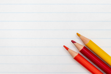 Colorful pencils on the background of a white lined sheet of notebook close-up with copy space