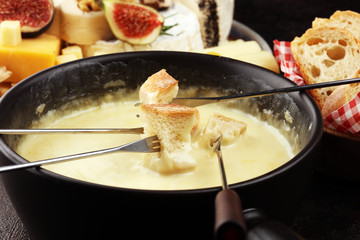 Gourmet Swiss fondue dinner on a winter evening with assorted cheeses on a board alongside a heated pot of cheese fondue with two forks dipping