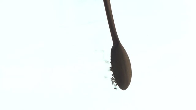 Top angle shot of cumin seeds poured from a wooden spoon against a white background