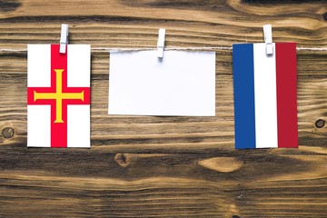 Hanging flags of Guernsey and Netherlands attached to rope with clothes pins with copy space on white note paper on wooden background.Diplomatic relations between countries.