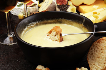 Gourmet Swiss fondue dinner on a winter evening with assorted cheeses on a board alongside a heated pot of cheese fondue with two forks dipping