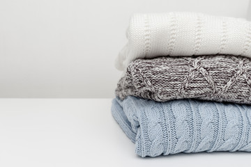 Fototapeta na wymiar Stack of cozy comfortable homely clean washed knitted pullovers in pastel colors, laundry and washing clothes concept. White background, copy space