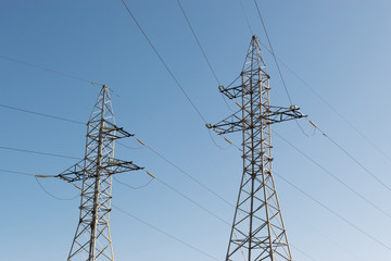 High-voltage technological power lines on metal poles with powerful power wires against the sky
