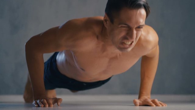 Young athletic thin man doing push-ups to failure during training in fitness gym. Workout training.