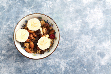 Bowl of granola with nuts, raisins and banana. Concept for a tasty and healthy meal. Rustic wooden background. Copy space. Top view. 