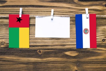 Hanging flags of Guinea Bissau and Paraguay attached to rope with clothes pins with copy space on white note paper on wooden background.Diplomatic relations between countries.