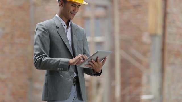male building designers or architech wearing helmets with tablet pc in front of unfinished brick house