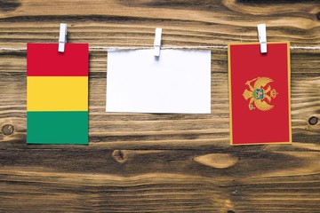 Hanging flags of Guinea and Montenegro attached to rope with clothes pins with copy space on white...