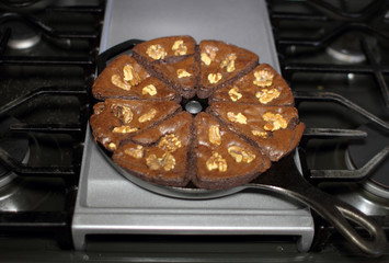Chocolate brownies with walnuts baked in a cast iron wedge pan, resting on the stove top in a home...