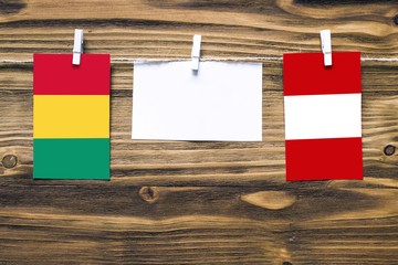 Hanging flags of Guinea and Peru attached to rope with clothes pins with copy space on white note paper on wooden background.Diplomatic relations between countries.