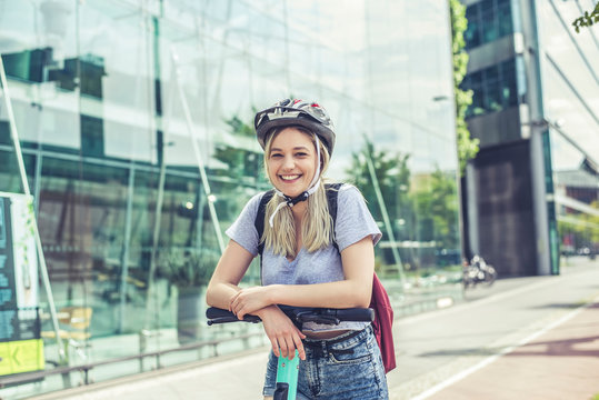 Portrait of happy young woman wearing cycling helmet leaning on handlebar of E-Scooter