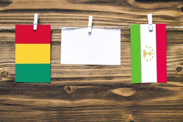 Hanging flags of Guinea and Tajikistan attached to rope with clothes pins with copy space on white note paper on wooden background.Diplomatic relations between countries.