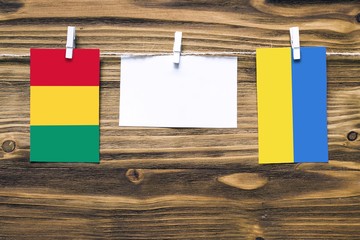 Hanging flags of Guinea and Ukraine attached to rope with clothes pins with copy space on white note paper on wooden background.Diplomatic relations between countries.