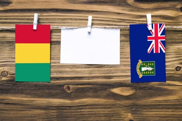 Hanging flags of Guinea and British Virgin Islands attached to rope with clothes pins with copy space on white note paper on wooden background.Diplomatic relations between countries.