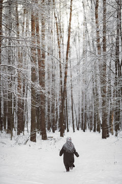 Back view of little girl wearing headscarf walking in winter forest