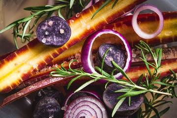 Autumn vegan food: halved purple haze carrots, purple onion rings, violet potatoes, rosemary