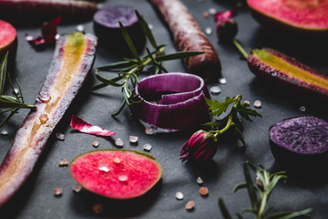 Fruit and vegetable set on black background: red moon apples, purple haze carrots, onion rings, rosemary, flowers
