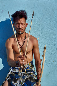 Tribal man with his traditional arch and arrows leaning on blue wall, Lubango, Angola