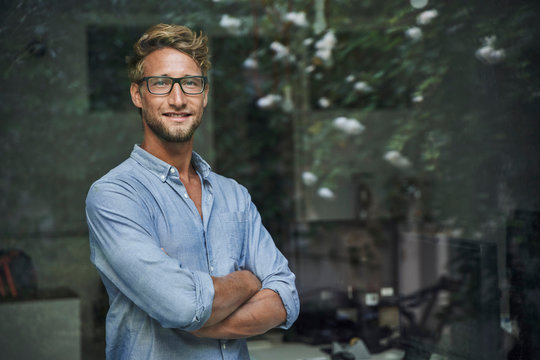 Portrait of casual young businessman behind windowpane in office