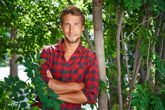 Portrait of confident young man wearing checkered shirt leaning against a tree