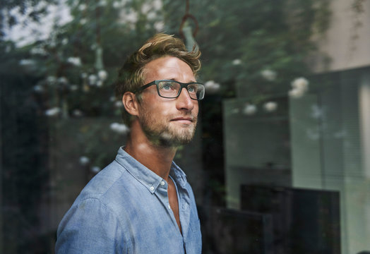 Casual young businessman behind windowpane in office