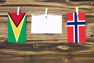 Hanging flags of Guyana and Norway attached to rope with clothes pins with copy space on white note paper on wooden background.Diplomatic relations between countries.