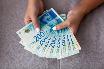 Woman's two hands holding a fan of money of Israeli New Shekels